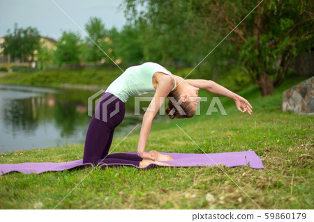 A young sports girl practices yoga on a green lawn A young sports girl practices yoga on a green lawn 59860179