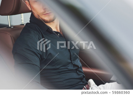 Beautiful young man in full suit while driving a car 59860360