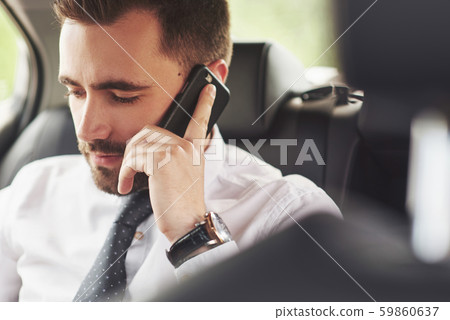 A businessman who sends a message to a smartphone and goes to the car's rear seat. 59860637