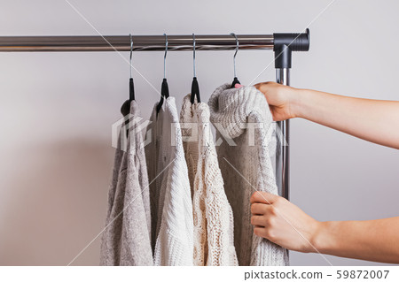 Woman choosing one of the warm knitted sweaters from her minimalist wardrobe. Woman choosing one of the warm knitted sweaters from her minimalist wardrobe. 59872007