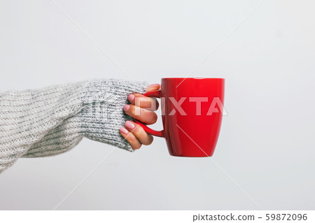 Woman's hand in cozy sweater holding a red coffee mug. 59872096