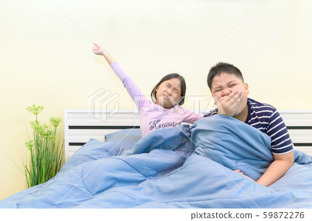 Brother is yawning and sister is stretching in bed 59872276