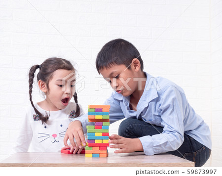 Two asian kid, boy and girl playing wooden blocks on wooden table and white wall background. Two asian kid, boy and girl playing wooden blocks on wooden table and white wall background. 59873997