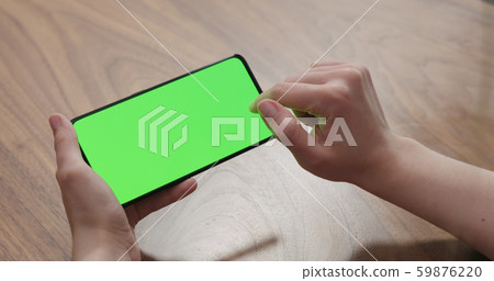 Young woman sitting at a table and using a smartphone with horizontal green screen 59876220