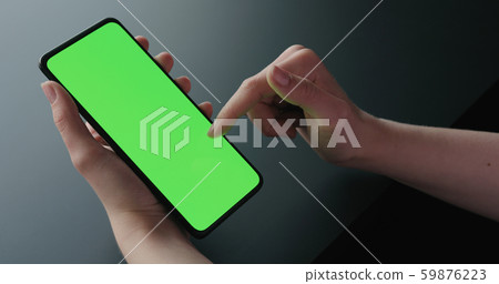 Young woman sitting on a chair near window and using smartphone with green screen Young woman sitting on a chair near window and using smartphone with green screen 59876223
