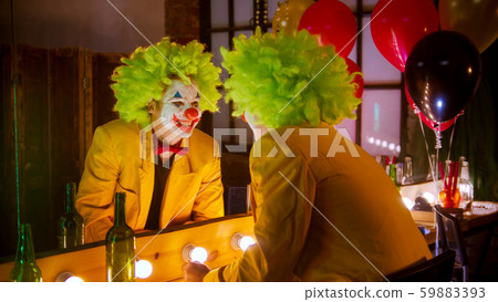 A crazy man clown in full costume looking in the mirror and smiling 59883393