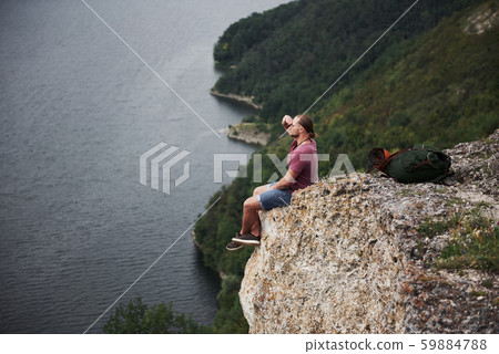 Traveller with backpack sitting on top of mountain enjoying view above the water surface. Traveling Traveller with backpack sitting on top of mountain enjoying view above the water surface. Traveling 59884788