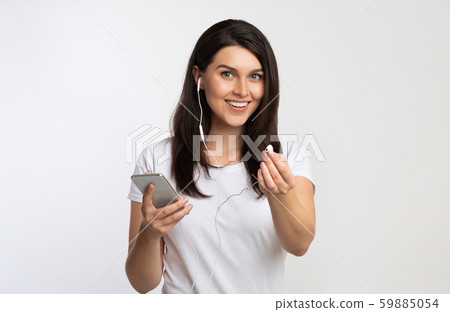 Girl Holding Smartphone Offering Earbud Listening To Music, White Background Girl Holding Smartphone Offering Earbud Listening To Music, White Background 59885054
