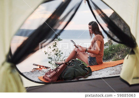 View from tent of woman traveller with backpack sitting on top of mountain enjoying view coast a View from tent of woman traveller with backpack sitting on top of mountain enjoying view coast a 59885063