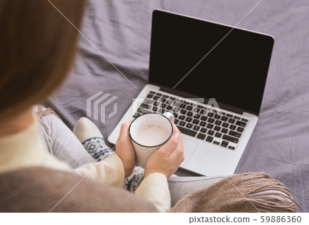 Girl with hot cocoa sitting on the bed and looking for Christmas gifts Girl with hot cocoa sitting on the bed and looking for Christmas gifts 59886360