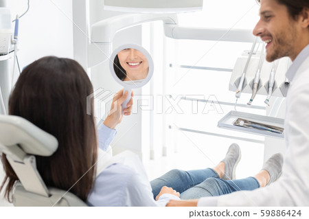 Sattisfied woman client of dental clinic smiling at mirror 59886424