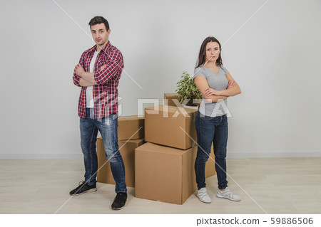Man and woman standing with hands folded, near stack of carton boxes in their new apartment. Man and woman standing with hands folded, near stack of carton boxes in their new apartment. 59886506