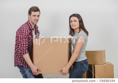 Young man and woman carrying a big heavy carton box togerher, making a great effort. Young man and woman carrying a big heavy carton box togerher, making a great effort. 59886584
