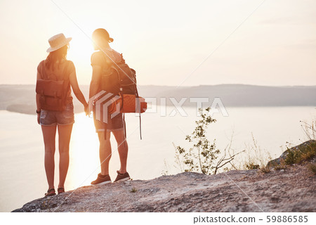 Two tourist male and woman with backpacks stand to the top of the crag and enjoying sunrise 59886585