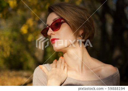 Young and beautiful girl with short hair and red fashionable sunglasses is posing against the trees Young and beautiful girl with short hair and red fashionable sunglasses is posing against the trees 59888194