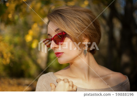 Young and beautiful girl with short hair and red fashionable sunglasses is posing against the trees 59888196