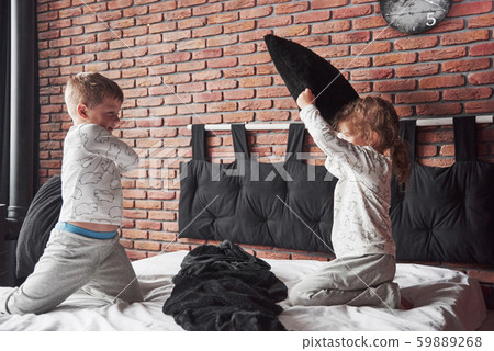 Naughty children Little boy and girl staged a pillow fight on the bed in the bedroom. They like that Naughty children Little boy and girl staged a pillow fight on the bed in the bedroom. They like that 59889268