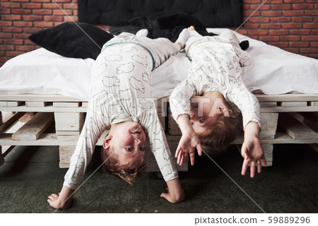 Happy kids playing in black bedroom. Little boy and girl, brother and sister play on the bed wearing 59889296