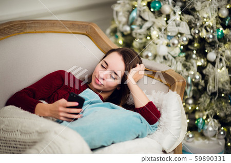 Young woman with mobile phone home lying on a sofa in front of fir tree 59890331