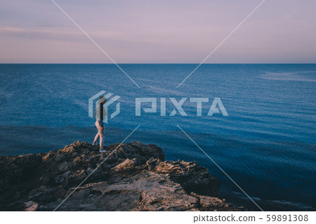 Woman traveler standing near sea on top of cliff in summer mountains and enjoying view of sea and nature. Cape Greco, Cyprus, Mediterranean Sea. Sunrise Woman traveler standing near sea on top of cliff in summer mountains and enjoying view of sea and nature. Cape Greco, Cyprus, Mediterranean Sea. Sunrise 59891308