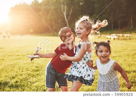 Brother and two sisters are playing together. Three children playing with a wooden airplane outdoor Brother and two sisters are playing together. Three children playing with a wooden airplane outdoor 59905928