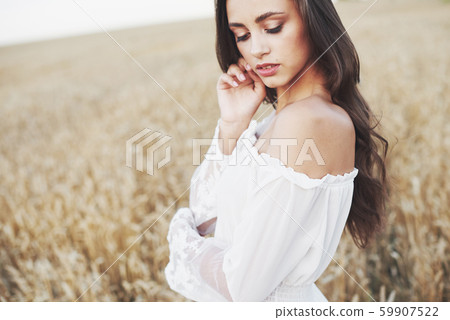 Young sensitive girl in white dress posing in a field of golden wheat Young sensitive girl in white dress posing in a field of golden wheat 59907522