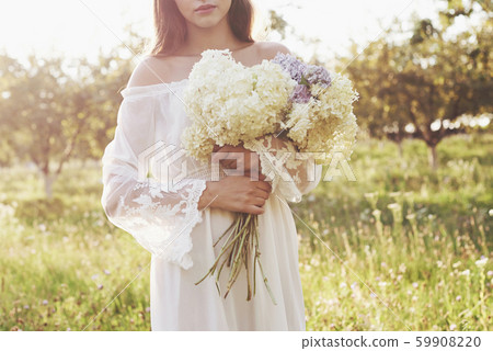 Beautiful young woman wearing elegant white dress and enjoying beautiful sunny afternoon in a summer 59908220