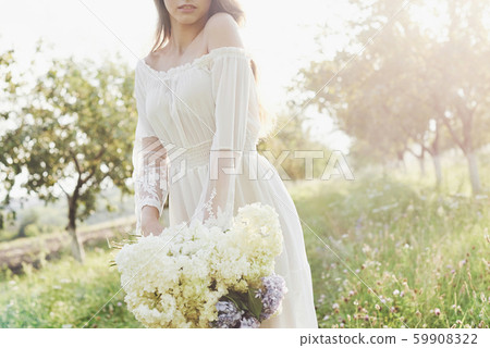 A beautiful young girl in a white light dress and a bouquet of summer flowers lays a fine day in the 59908322