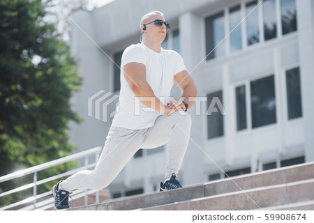 A handsome fitness man in a sportswear, doing stretching while preparing for serious exercise in the A handsome fitness man in a sportswear, doing stretching while preparing for serious exercise in the 59908674