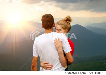 Loving girl is sad while saying goodbye and hugs a young guy in the mountains during sunset. Loving girl is sad while saying goodbye and hugs a young guy in the mountains during sunset. 59910045