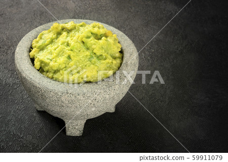 Guacamole in a molcajete, Mexican avocado dip sauce in the traditional stone mortar, on a dark 59911079