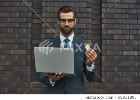 Our future. Handsome businessman in formal wear and eyeglasses holding laptop and bitcoin in another 59911903