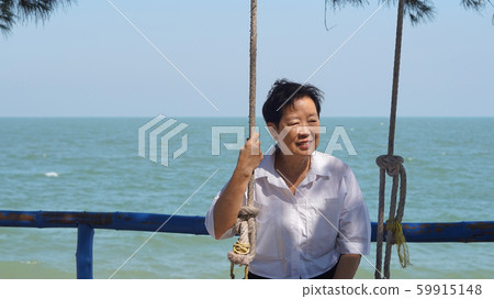 Asian senior woman alone at sea sunrise thinking Asian senior woman alone at sea sunrise thinking 59915148