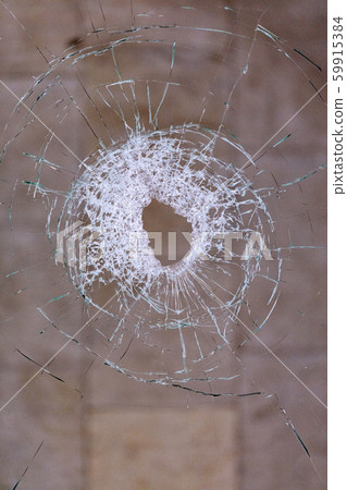 Hole in broken glass on a dark beige background. Hole in broken glass on a dark beige background. 59915384