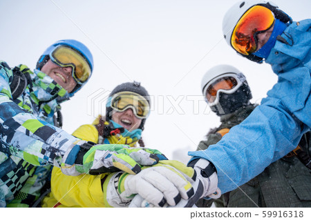 Photo from bottom of four happy snowboarders in helmet doing handshake on blue sky. Photo from bottom of four happy snowboarders in helmet doing handshake on blue sky. 59916318