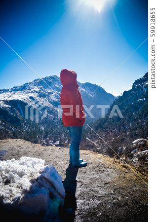 A woman in winter warm clothing standing on top of the rock of a snowcapped rocky mountain peak. 59918655