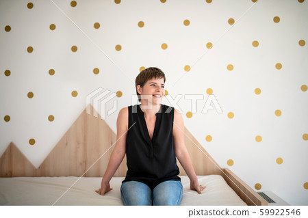 Front view of young woman sitting on bed in bedroom indoors at home. Front view of young woman sitting on bed in bedroom indoors at home. 59922546