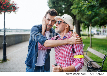 Young man and blind senior with white cane walking on pavement in city. 59922664