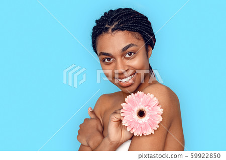 Beauty Concept. Young african woman isolated on blue with flower posing to camera smiling cheerful Beauty Concept. Young african woman isolated on blue with flower posing to camera smiling cheerful 59922850