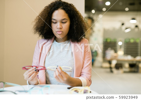 Mixed-race curly girl cannot decide which pair of new eyeglasses to buy 59923949