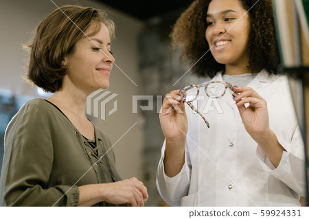 Confident mixed-race consultant showing new model of eyeglasses to young client 59924331