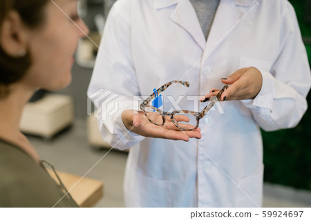 Hands of consultant or clinician in whitecoat holding new stylish eyeglasses Hands of consultant or clinician in whitecoat holding new stylish eyeglasses 59924697