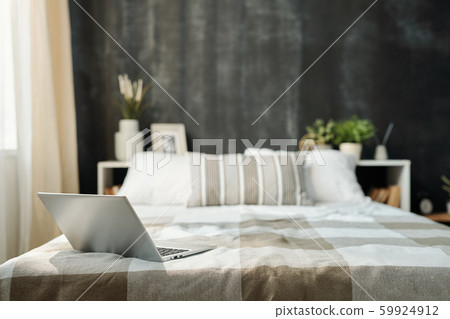 Open laptop on neatly made bed with linen checkered plaid and pillows 59924912