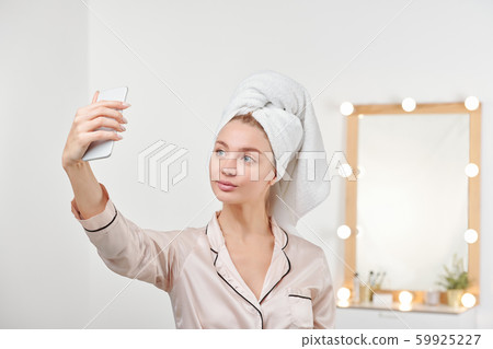 Fresh young female in silk pajamas making selfie by mirror after shower Fresh young female in silk pajamas making selfie by mirror after shower 59925227