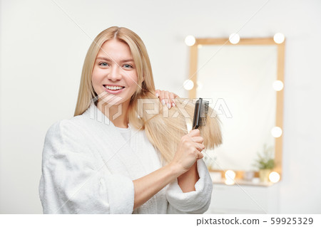 Happy and healthy young woman with toothy smile brushing her long blond hair Happy and healthy young woman with toothy smile brushing her long blond hair 59925329