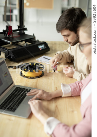 Young man with nippers bending over table while cutting piece of yellow filament 59925604