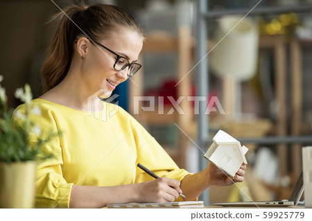 Successful young female architect with house model in hand looking through notes Successful young female architect with house model in hand looking through notes 59925779