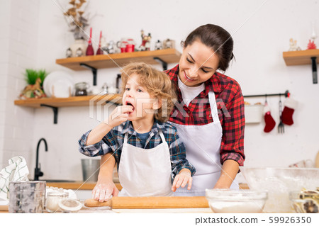 Cute little boy tasting homemade dough while helping mom to roll it on table Cute little boy tasting homemade dough while helping mom to roll it on table 59926350