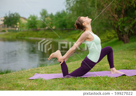 A young sports girl practices yoga on a green lawn A young sports girl practices yoga on a green lawn 59927022