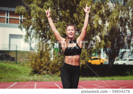 Happy woman with earphones running on racetrack 59934278
